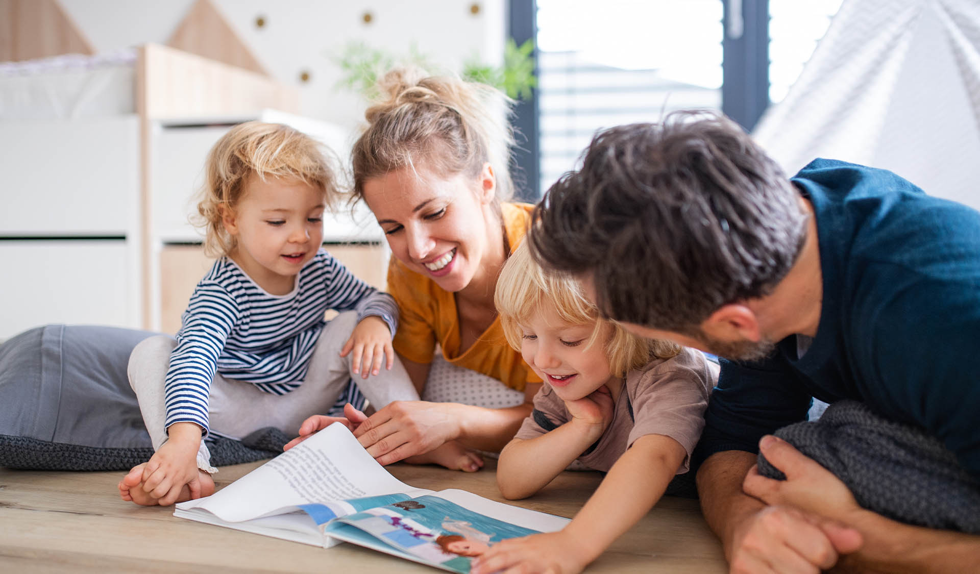 Young family with two small children indoors in bedroom reading a book