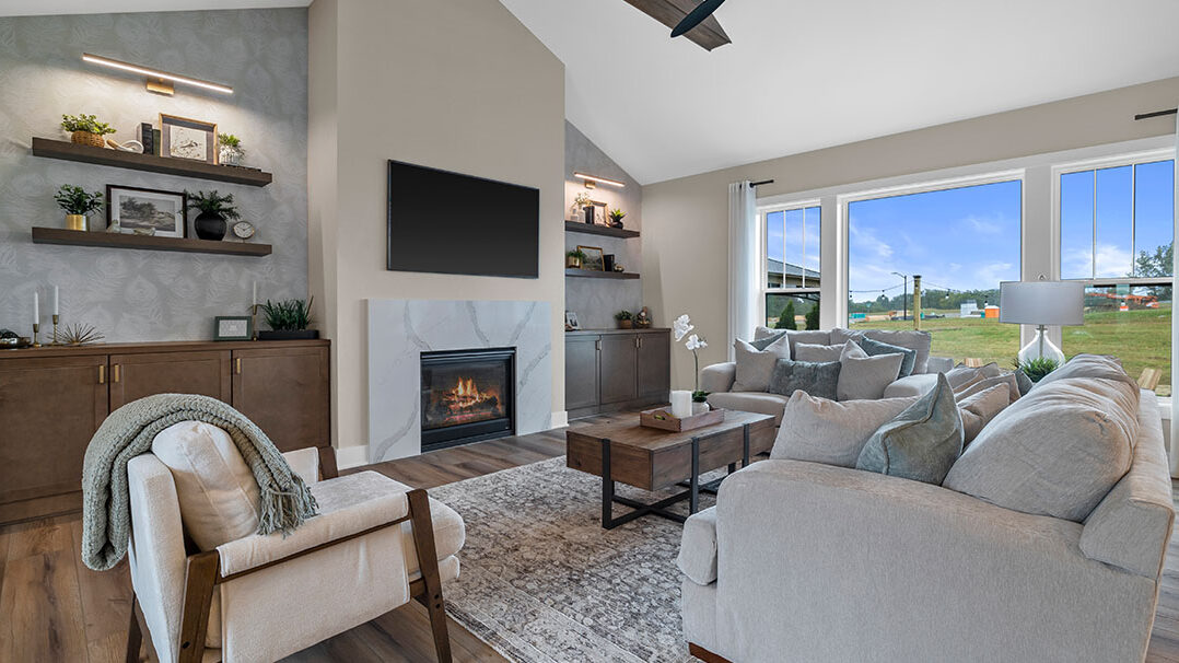 Parade of Homes model, The Lexi, great room with large grey couches and welcoming warm fireplace. Featuring two built-in with showcase personal items