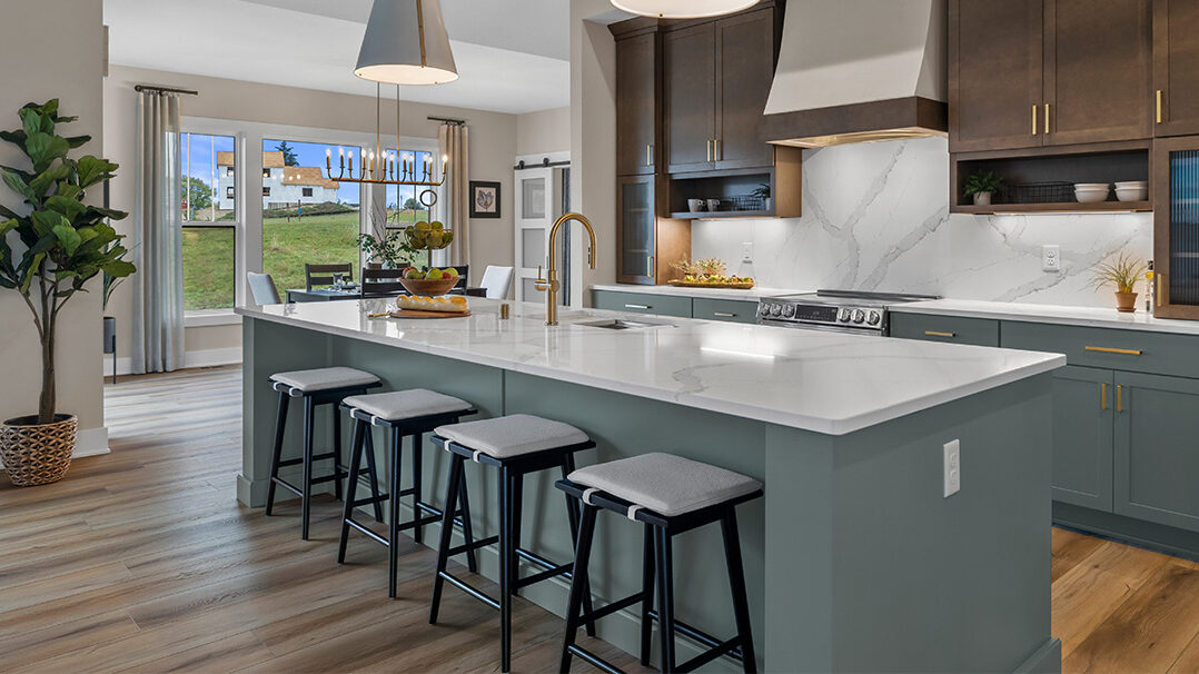 Parade of Homes model, The Lexi, kitchen featuring bright white counter tops, dark green grey lowers, and wood uppers. All the fine details feature bright gold.