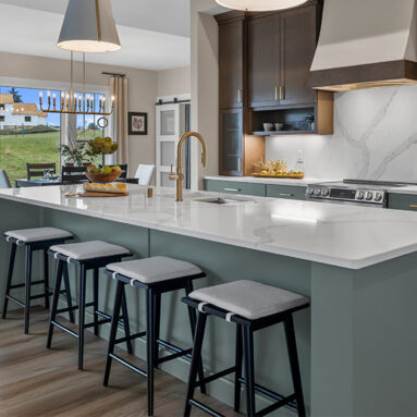 Parade of Homes model, The Lexi, kitchen featuring bright white counter tops, dark green grey lowers, and wood uppers. All the fine details feature bright gold.