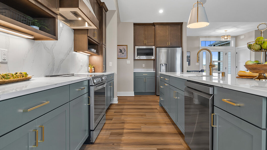 Parade of Homes model, The Lexi, kitchen featuring bright white counter tops, dark green grey lowers, and wood uppers. All the fine details feature bright gold.